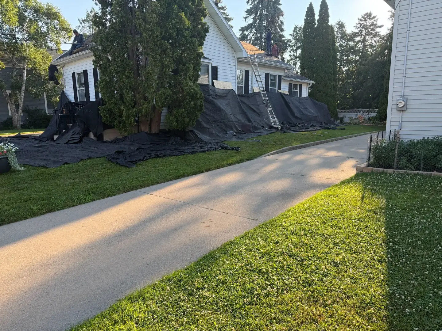 Everything around the house gets covered before a single shingle comes off. Tear-off debris is mostly nails, and this is how the beds and the lawn stay out of it.